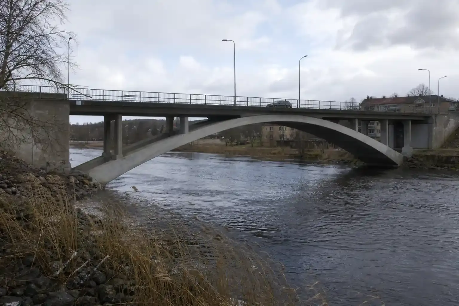 Bågbro av betong över en älv med vägtrafik på brobanan