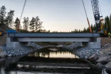 Kran lyfter en stålbalk över ett smalt vattendrag mellan betongstöd