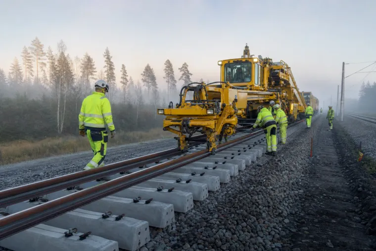 Banarbetare och en gul spårmaskin vid nylagda betongsliprar