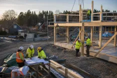 Bygglag samlas kring ritningar vid en trästomme under uppförande