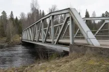 Fackverksbro av nitat stål över ett vattendrag i skogsmiljö
