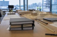 Detaljerad byggmodell och pärmar på ett bord framför stora fönster