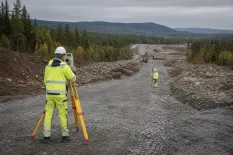 Mättekniker arbetar med stativ på en ny vägsträckning genom skogslandskap