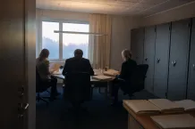 Tre personer håller möte i ett avskilt kontor med dokumentskåp